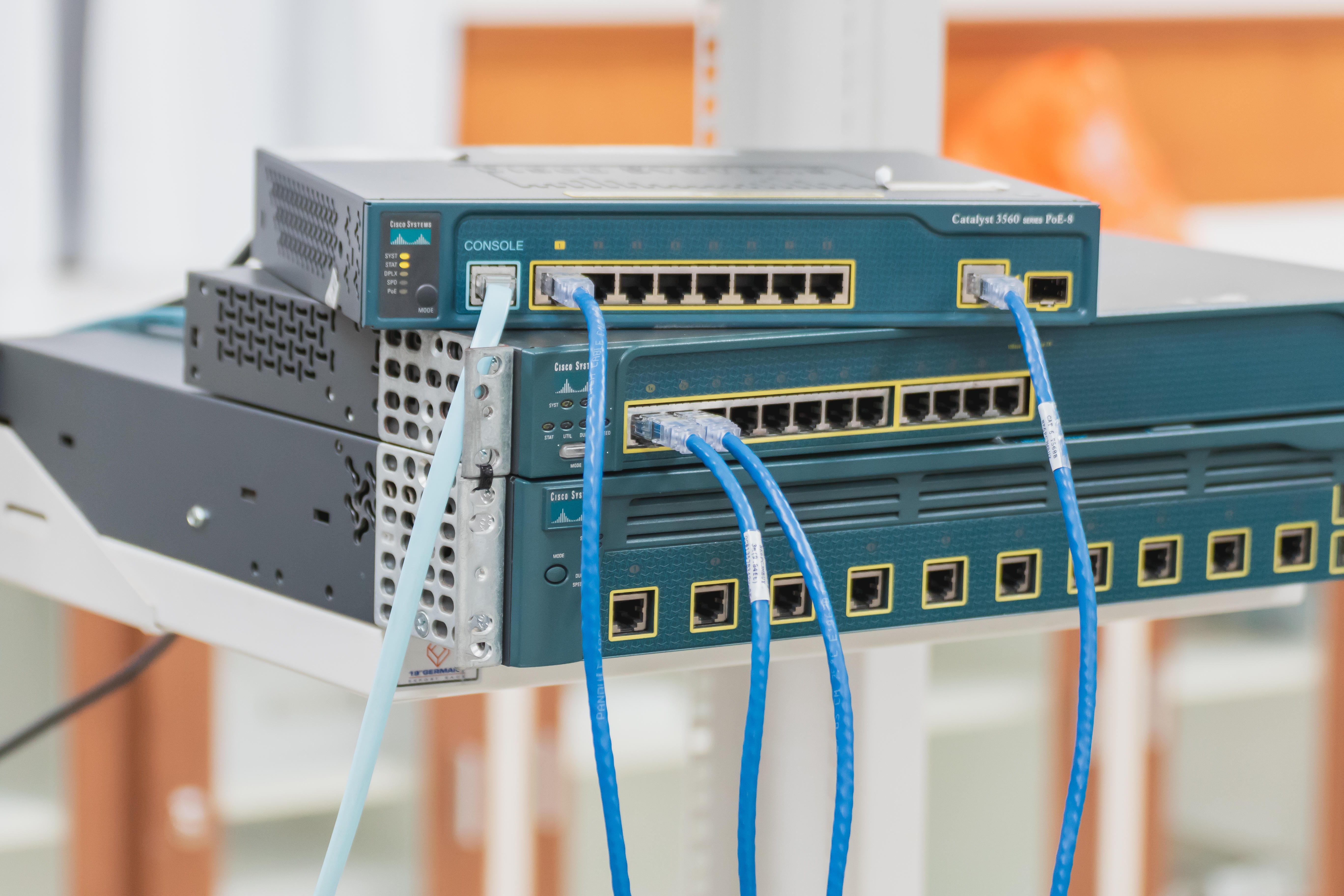 Cisco enterprise rack RJ45 LAN switches installed on a server rack in a server room of a company with several LAN cable pluggin into its socket