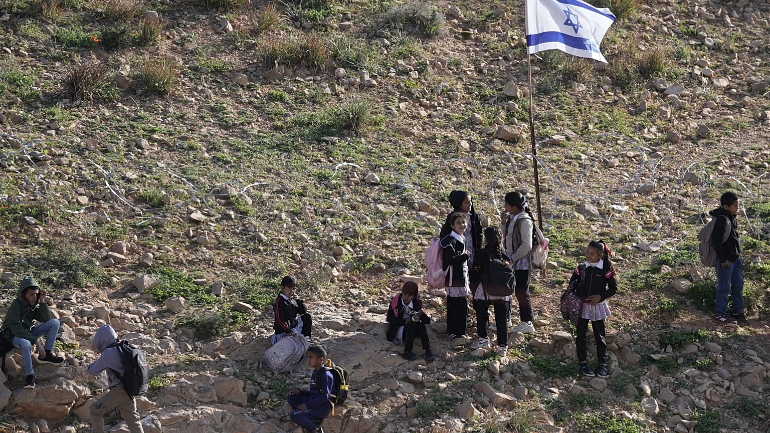 طلاب فلسطينيون يسيرون إلى المدرسة على طول سياج يفصل قريتهم عن مستوطنة الكرمل الإسرائيلية القريبة
