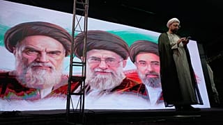 رجل دين يقف على منصة أمام صور آية الله روح الله الخميني وعلي خامنئي  ومجتبى خامنئي، طهران، 7 يونيو 2026.