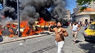 Pessoas correm em frente a carros queimados atingidos por um ataque aéreo israelita na cidade portuária de Sídon, no sul do Líbano, 10 de junho de 2026.