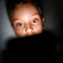 Symbolfoto: Gestellte Aufnahme zum Thema Mediennutzung bei Kindern. Ein Kind schaut im Dunkeln auf das Display eines Smartphones