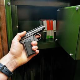 Jemand hält eine kleine Handfeuerwaffe vor einem Tresor für die sichere Aufbewahrung