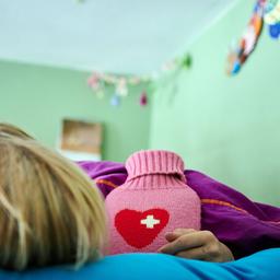 Ein krankes Kind liegt mit Wärmflasche im Bett
