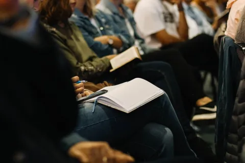 Looking along a row of people at a seminar. We can't see their faces. Some of them are taking notes.