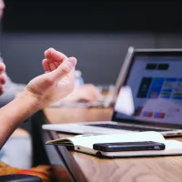 Laptop on a table with notepad and phone, user's hands in foreground 