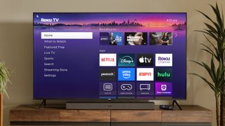 A 2025 Roku TV on a credenza displaying the Roku OS home screen, which showcases various streaming app icons