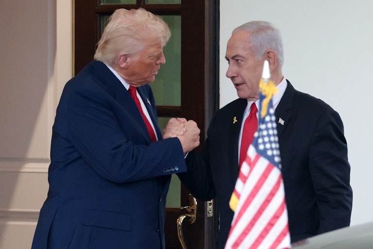 Trump and Netanyahu clasp hands standing behind an American flag
