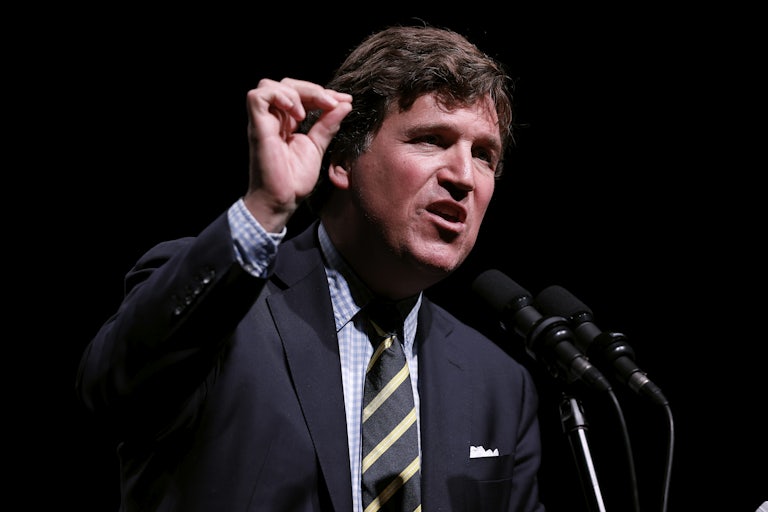 Tucker Carlson speaks into a mic and makes a hand gesture for emphasis.