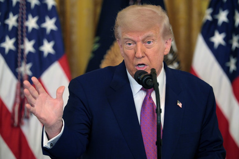 Donald Trump speaking at a mic. Two U.S. flags are behind him.
