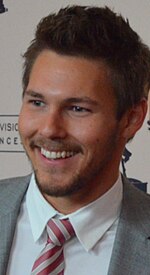 A man with dark hair wearing a grey suite including a red and grey pattern tie