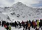 Photographie couleur d’une montagne complètement enneigée en arrière-plan, de nombreuses personnes l’observant au premier plan.