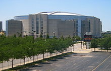 Photographie extérieure du United Center derrière une route bordée d'arbres.