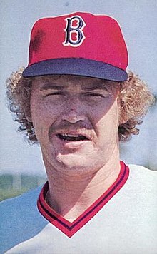 A man in a white baseball uniform and red cap