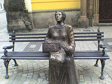 Statue en bronze d'une femme assise sur un banc, dans la rue