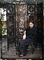 A Vietnamese lady sitting by a folding screen.