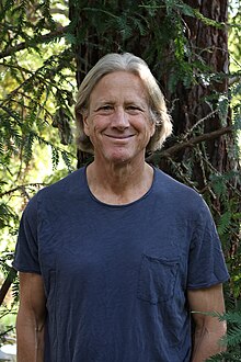 Dacher Keltner, wearing a blue t-shirt by a Redwood tree, smiling at the camera