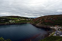 Cuan ar lá maith. Roinnt tithe le feiceáil agus maolchnoic os cionn an chuain.