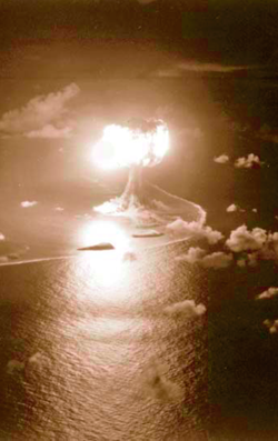 An atomic explosion lights up the night sky over a coral atoll