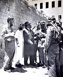 Black and white photo of several Jews and Jordanians talking in front of an ancient wall