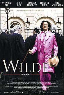 A man in a pink suit. Behind him, several judges wearing their white wigs and black cloaks, their backs turned.