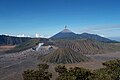 Vulcanul Bromo (craterul mare în stânga), in fundal se poate observa erupţia vulcanului Semeru.