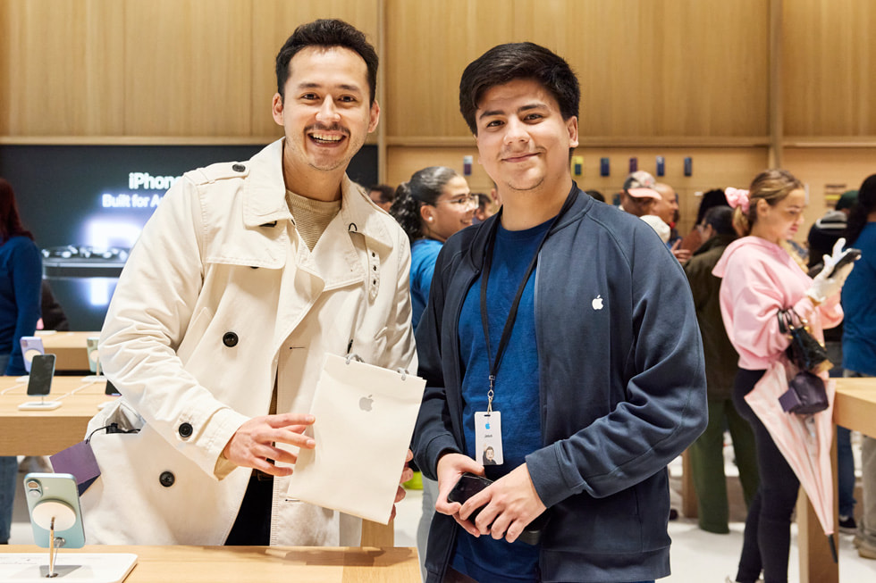 Seorang pelanggan yang memegang tas Apple berdiri di samping anggota tim Apple di Apple Miami Worldcenter.