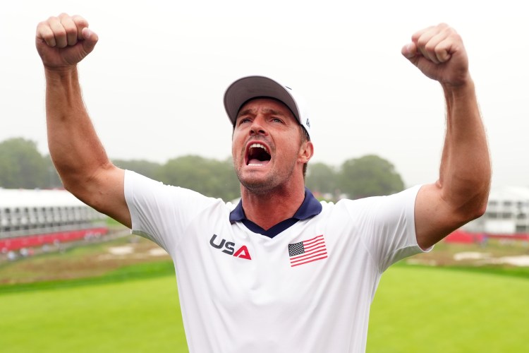 Bryson DeChambeau of Team United States on the 18th green at the Bethpage Black Course with his arms raised in celebration.