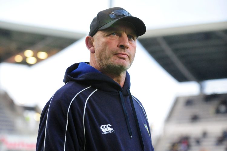 Vern Cotter wearing a black cap and blue hoodie, holding a rugby ball.